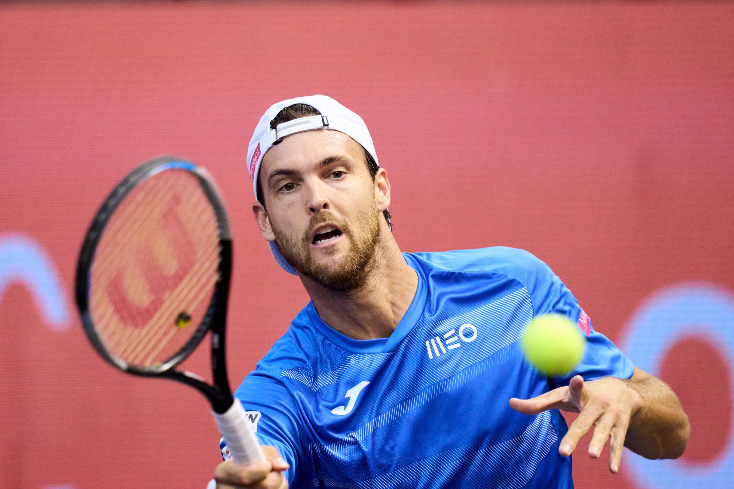 João Sousa um dos maiores tenistas portugueses de sempre a jogar uma partida de ténis com um boné branco e camisola azul